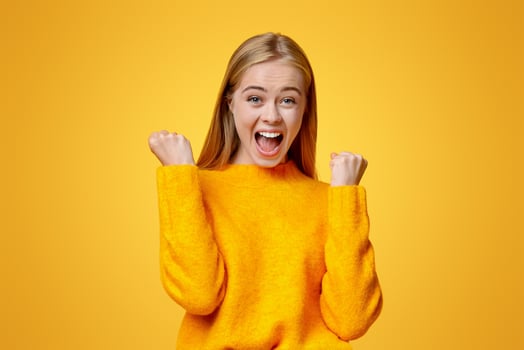 Emotional teen girl shouting and raising clenched fists in the air, rejoicing success over orange studio background photo