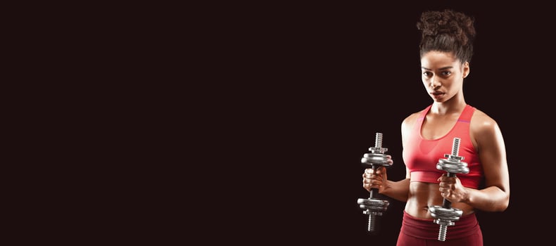 Afro woman fitness model having work out with barbells over black background, empty space photo