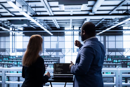 Manager overseeing data center next to employee, doing yearly infrastructure inspection. Coworkers doing brainstorming in server farm, monitoring supercomputers equipment with laptop photo