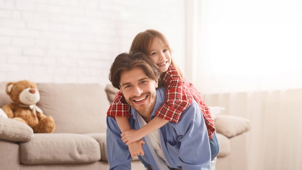 Father and daughter spending weekend together at home. Little girl riding fathers back in kid bedroom, copy space photo