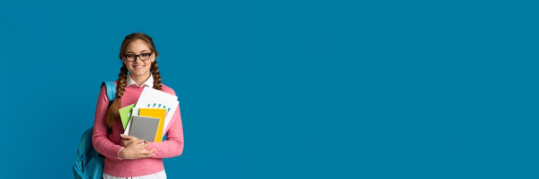 Modern student concept. Cute smiling girl teenager with notebooks and backpack posing on blue studio background, copy space photo