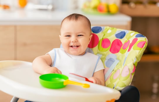 A happy baby sits in a high chair, smiling and playing with colorful toys. The modern kitchen setting provides a bright and joyful atmosphere. photo
