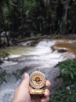 Close up of compass in woman hand with waterfall as background. The concept of world tourism day, Searching the right directions and Travel photo
