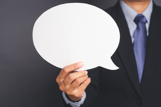Businessman in suit holding an empty speech bubble standing against a gray background photo