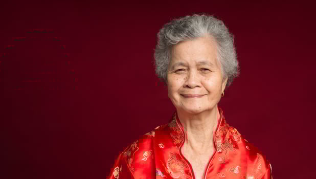 A senior Asian woman wearing a traditional cheongsam qipao dress looking at the camera with a smile while standing against a red background photo
