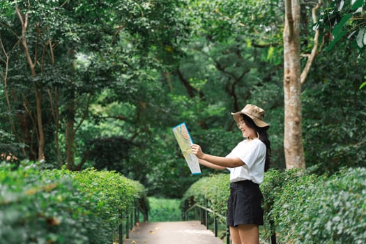 Woman with hat holding a map in the forest. Happy woman hiking and looking at map outdoors in nature. photo