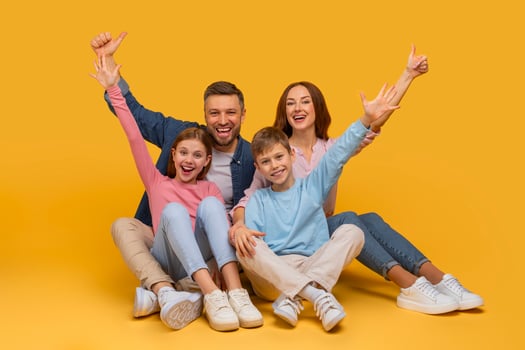A joyful family sits closely together with arms raised in a celebratory gesture, smiling enthusiastically. A father and mother are behind their daughter and son, all sharing a moment of happiness photo
