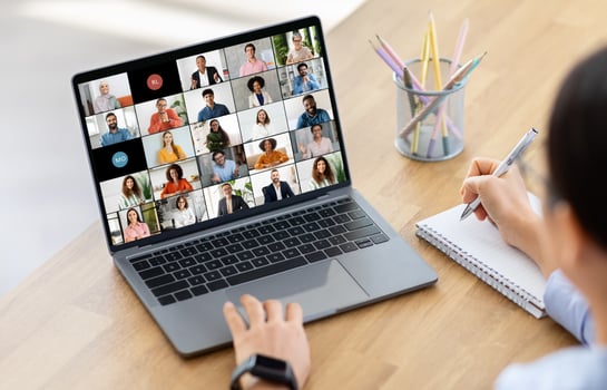 Woman manager sits at a wooden desk with a laptop computer open in front of them. The screen shows a conference with multiple participants. photo