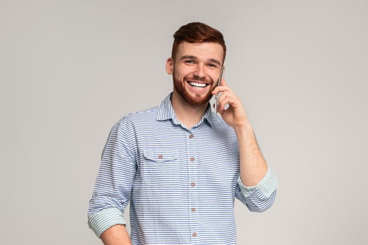 Happy Millennial Guy Talking On Mobile Phone And Smiling at Camera, grey studio background, free space photo