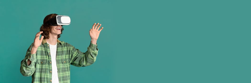 Modern entertainment concept. Young guy in virtual reality headset playing games on turquoise background, copy space photo