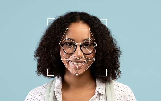 A young African American woman with curly hair and glasses smiles at the camera, showcasing a facial recognition overlay against a soothing blue background. photo