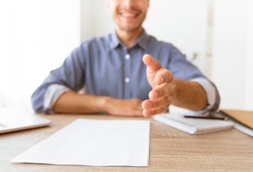 A man sitting at a desk extends his hand for a handshake, with a smile on his face. photo