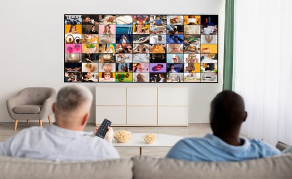 Two people are sitting on a couch in a living room, watching a large television screen displaying a multitude of smaller screens. They appear to be engrossed in the content displayed on the television photo