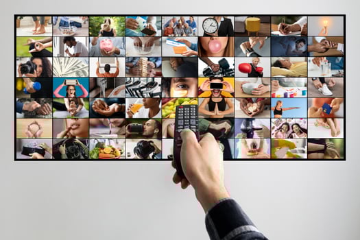 A persons hand is shown holding a remote control, pointing at a television screen. The television screen displays a collage of various images, each depicting a different activity or scene. photo