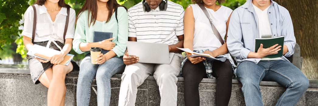 Preparing For Classes Outdoors. Diverce university students sitting outside with laptop and workbooks, studying together, cropped image, panorama photo