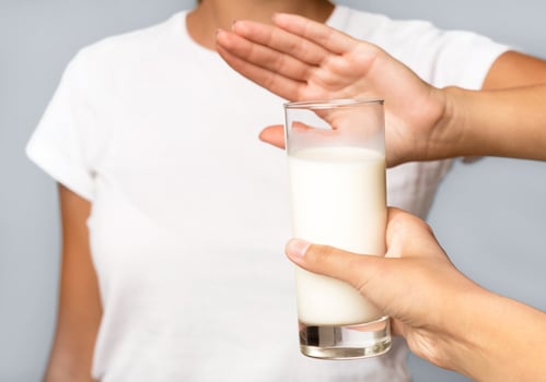 Lactose Intolerance. Unrecognizable Girl Gesturing No To Glass Of Milk Standing Over White Studio Background. Cropped photo