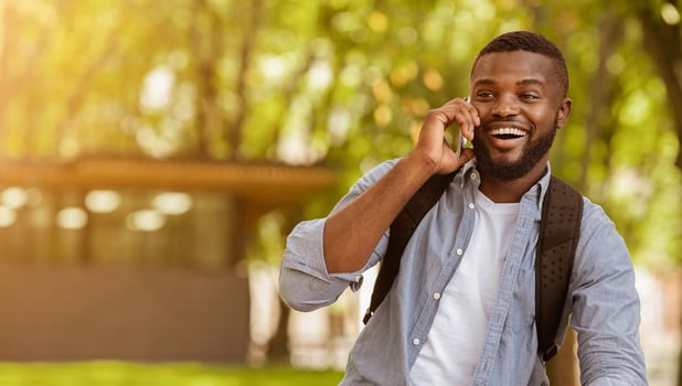 Nice to hear you. Cheerful african american guy having pleasant phone call outdoors, panorama with copy space photo