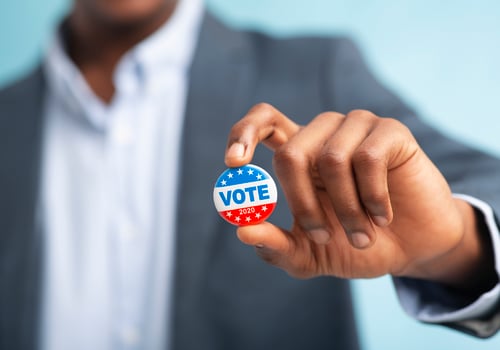 African man holding vote button on blue background for the November elections in the United States 2020, blurred photo