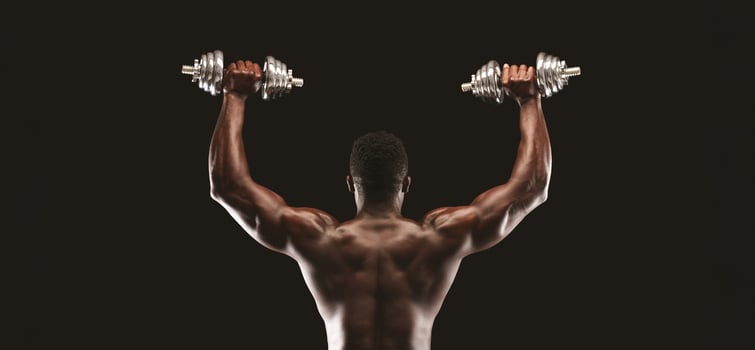 A muscular man lifts two dumbbells above his head, showing off his back muscles. photo
