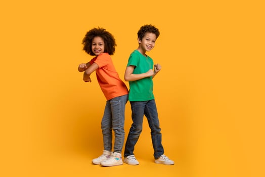 A pair of joyful African American children, a boy and a girl, are standing back to back with confident smiles on their faces, dancing on yellow background photo