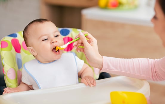 A mother and her baby boy are sharing mealtime in the kitchen, with the baby in a high chair. The atmosphere is nurturing and intimate, reflecting family warmth. photo
