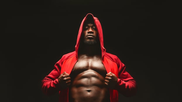 Confident african bodybuilder in red hooded shirt with bare chest, black studio background photo