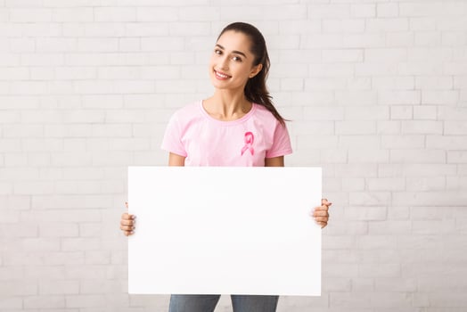 Breast Cancer Volunteer Woman In Pink T-Shirt Holding Empty White Board Standing Against Wall Indoor. Empty Space, Mockup photo