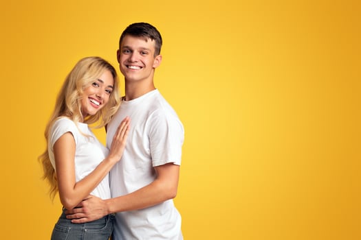 Portrait of happy young couple hugging and smiling at camera over yellow background, copy space photo