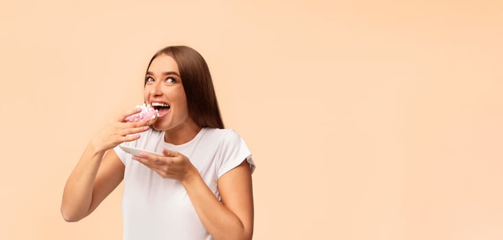 Hungry Pregnant Woman Eating Donut Standing On White Background. Studio Shot, Panorama With Copy Space photo