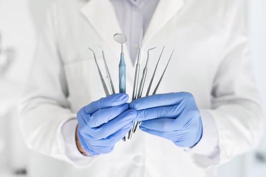 Doctor with blue gloves holding set of metal medical equipment tools for dental care, cropped photo