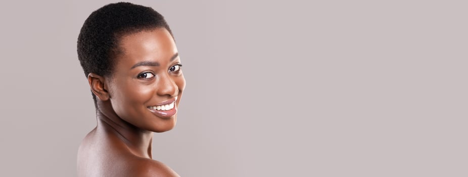 Beauty portrait. Beautiful black woman with short hair, white smile and clean glowing skin over grey studio background, copy space photo