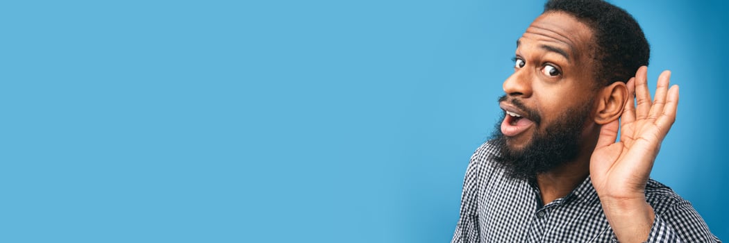 Eavesdropping Concept. Closeup of black guy holding hand near his ear and listening carefully isolated over blue wall, panorama with copy space photo