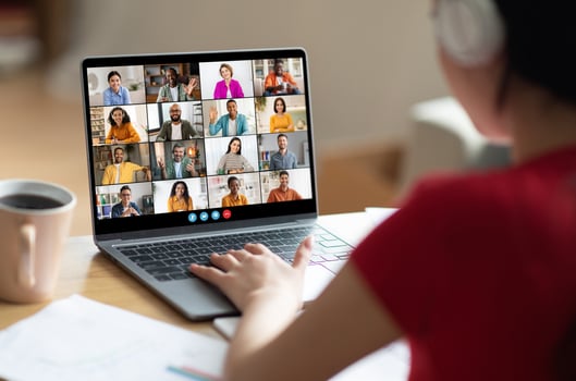 A woman in a red shirt participates in a large online conference meeting on her laptop. Her hands are on the trackpad, and she is looking at the screen with a focused expression. photo