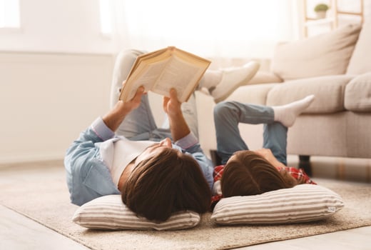 Little daughter and daddy enjoying time together, laying on floor at home, man reading book to his cute daughter, empty space photo