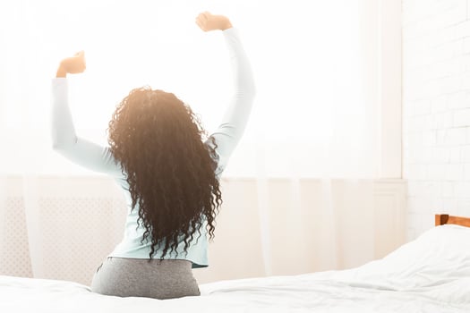 Young well-rested african woman stretching on bed, enjoying new day, back view, copy space photo