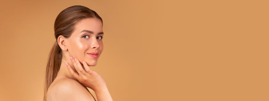 Beauty and fashion. Sexy young lady with silky hair and soft skin touching her face on beige background, copy space photo