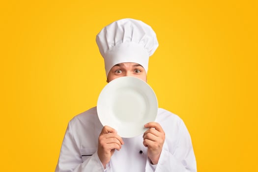 Funny Chef Guy Peeking Out Of Plate Looking At Camera Standing In Studio Over Yellow Background. Panorama photo
