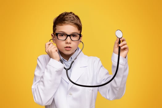 Actual game. Little boy in medical uniform playing with stethoscope, orange panorama background with free space photo