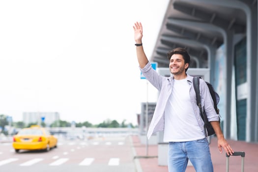 Young guy standing near airport, raising hand and trying to stop car, empty space photo