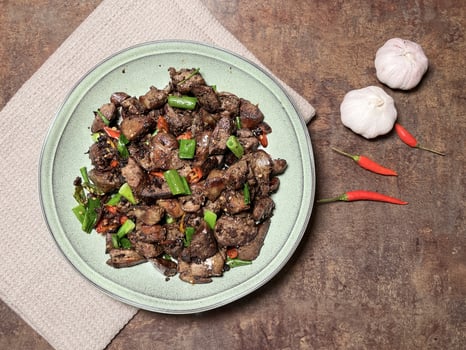 Tumis Ati Goreng is a popular Indonesian stir-fried chicken liver dish known for its rich, savory flavors and spicy kick served on a plate with rustic background. Top view photo