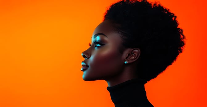 A woman with a short, curly black hairstyle is standing in front of an orange background. The woman's face is the main focus of the image, and she is looking straight ahead photo