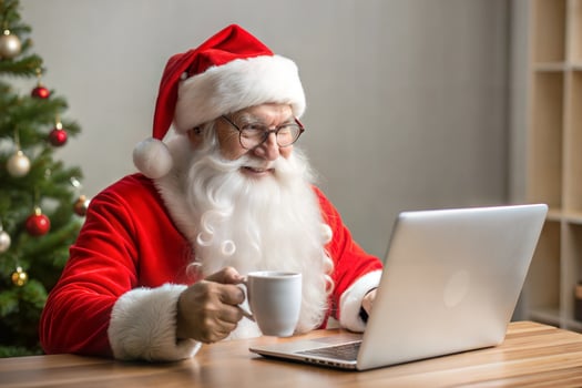 A man in a Santa hat is sitting at a desk with a laptop and a cup of coffee. photo