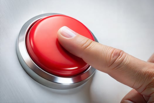 A red button is being pressed by a person's finger. The button is located on a wall and is surrounded by a silver frame. Concept of urgency or importance. photo