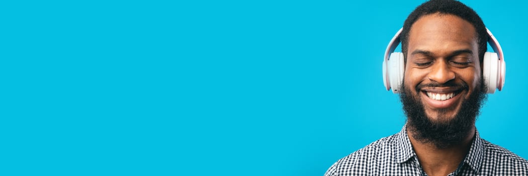 Perfect Song. Closeup portrait of smiling african american guy listening to music or podcast in headset isolated on blue studio wall, panorama with copy space photo