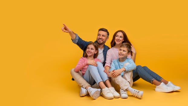 A joyful family is sitting closely with a father pointing at something out of frame, creating a moment of togetherness and curiosity, pointing at copy space on yellow background photo