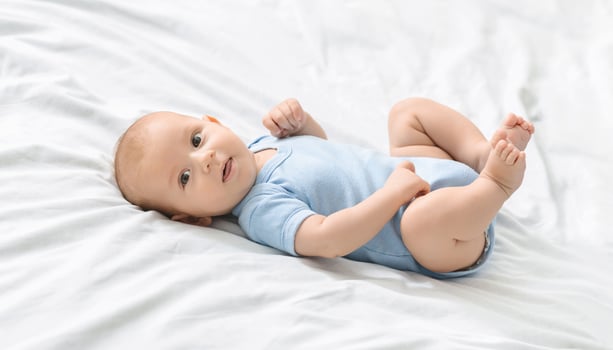 Portrait of cute newborn baby lying on bed in blue bodysuit, copy space photo