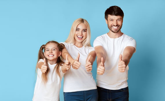 A happy family of three, a father, a mother, and a daughter, all wearing white t-shirts, stand together against a blue background, smiling and giving thumbs up. photo