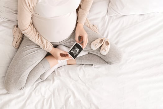 Pregnant woman looking at her baby sonography, enjoying future motherhood with first photo of her unborn child and tiny shoes, top view with free space