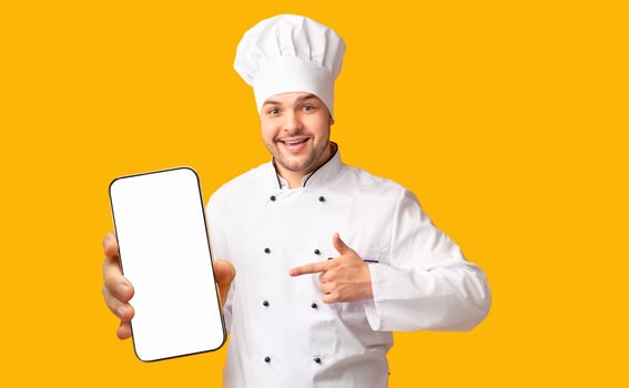Positive Chef Man Pointing Finger Showing Empty White Board In His Hands Standing Over Yellow Studio Background. Mockup photo