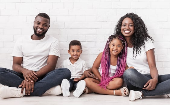 Family love and care. Smiling black parents with their two little kids sitting on floor together and looking at camera over white wall background photo